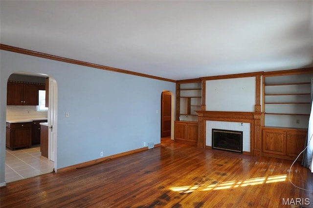 1014 Jefferson St, Hermann, MO 65041 - unfurnished living room with arched walkways, light wood finished floors, crown molding, a fireplace, and built in features