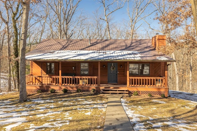 rustic home with covered porch, metal roof, and a chimney