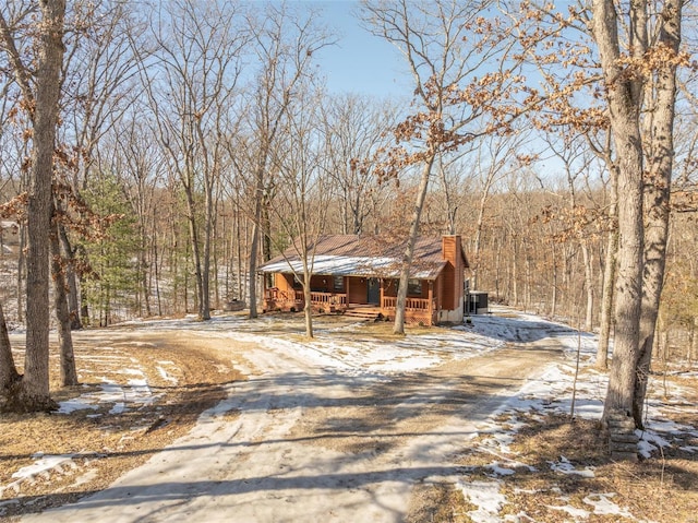 chalet / cabin featuring a porch, dirt driveway, and a chimney