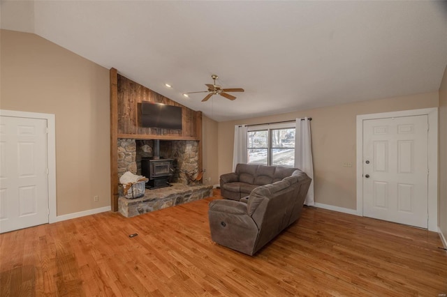 living area with a wood stove, lofted ceiling, a ceiling fan, light wood finished floors, and baseboards