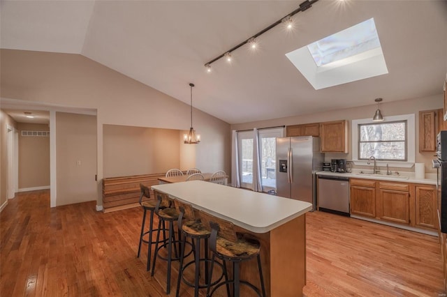 kitchen with stainless steel appliances, a sink, lofted ceiling, light wood finished floors, and a breakfast bar