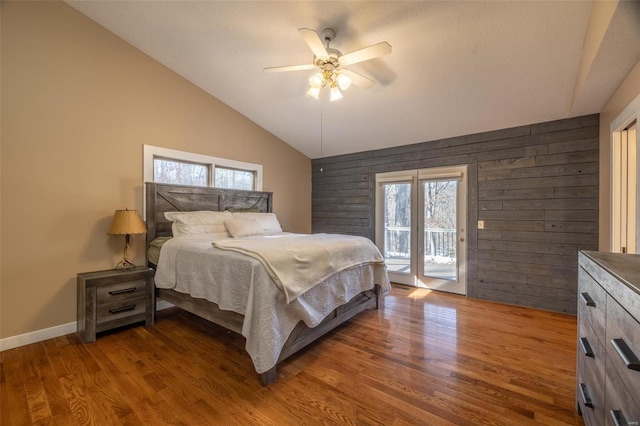 bedroom featuring access to outside, wood finished floors, lofted ceiling, wooden walls, and ceiling fan