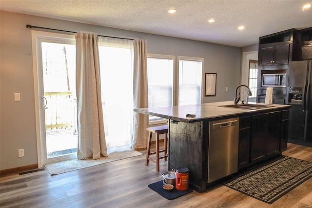 kitchen featuring stainless steel appliances, a sink, a kitchen island with sink, light wood-type flooring, and a breakfast bar