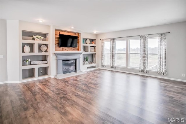 unfurnished living room featuring a glass covered fireplace, wood finished floors, built in features, baseboards, and recessed lighting
