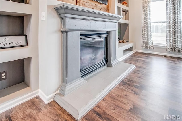 detailed view of wood finished floors, baseboards, and a glass covered fireplace
