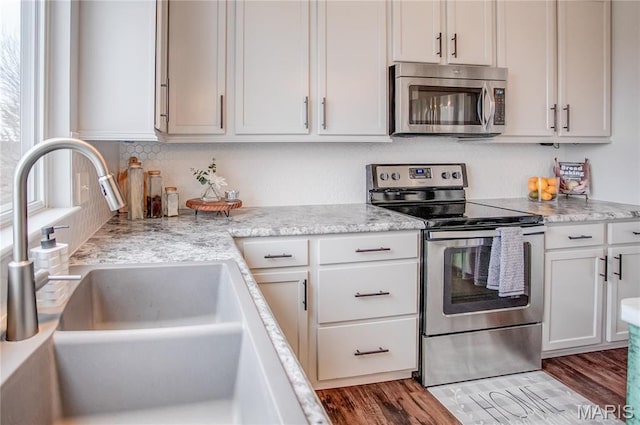 kitchen with appliances with stainless steel finishes, a sink, wood finished floors, and white cabinetry