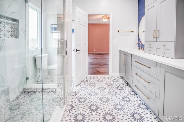 bathroom featuring a marble finish shower, toilet, vanity, a ceiling fan, and baseboards