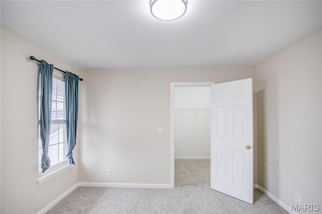 unfurnished bedroom with carpet flooring, a walk in closet, baseboards, and a closet