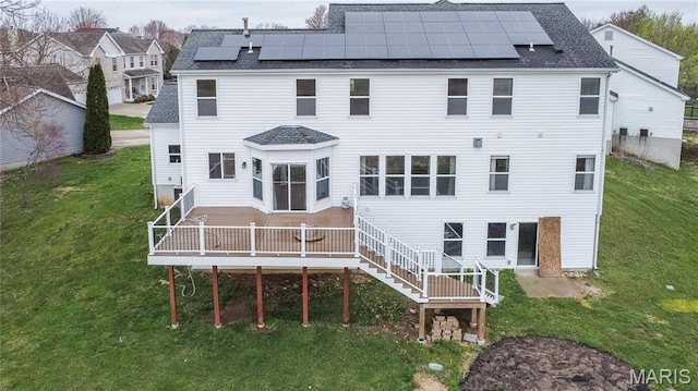 rear view of house with roof with shingles, solar panels, a yard, and a deck