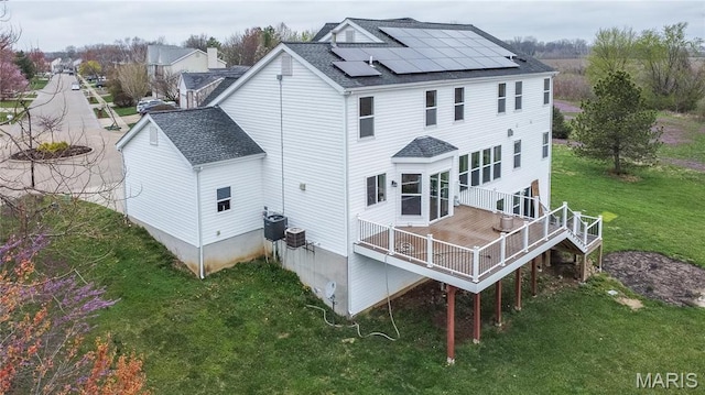back of house with a shingled roof, roof mounted solar panels, a yard, a deck, and central AC unit