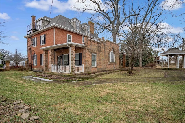 view of side of home with brick siding, a yard, a balcony, a gazebo, and a chimney