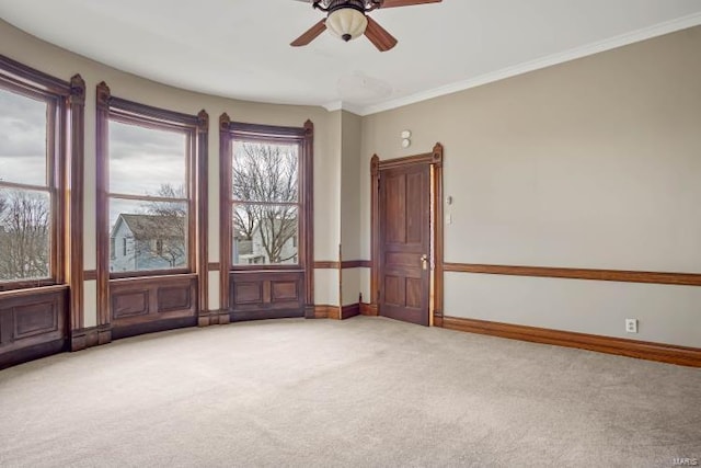 spare room with light colored carpet, a ceiling fan, baseboards, and ornamental molding
