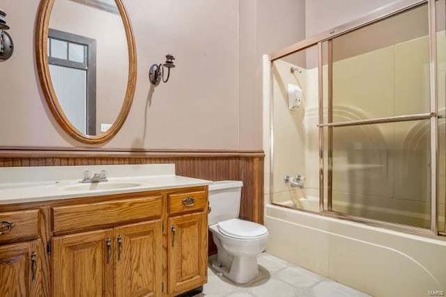 full bathroom featuring toilet, vanity, wainscoting, and combined bath / shower with glass door