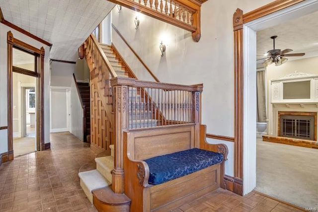 staircase featuring ceiling fan, baseboards, a glass covered fireplace, and crown molding