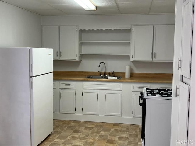 kitchen with freestanding refrigerator, gas range, a sink, white cabinetry, and open shelves