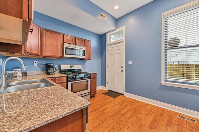 4125 Chouteau Ave, Saint Louis, MO 63110 - kitchen with appliances with stainless steel finishes, a sink, brown cabinetry, baseboards, and light wood-style flooring