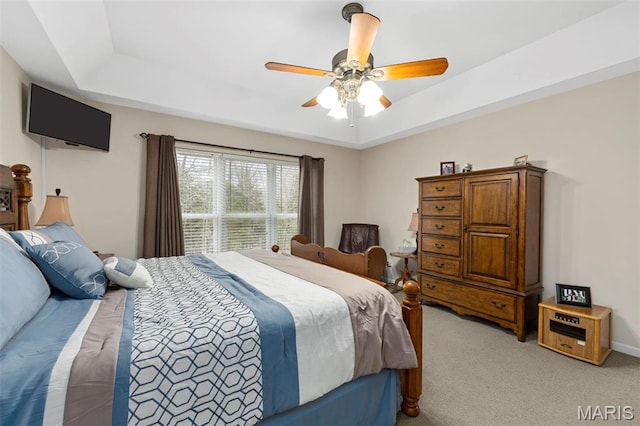 bedroom featuring a raised ceiling, light colored carpet, and ceiling fan