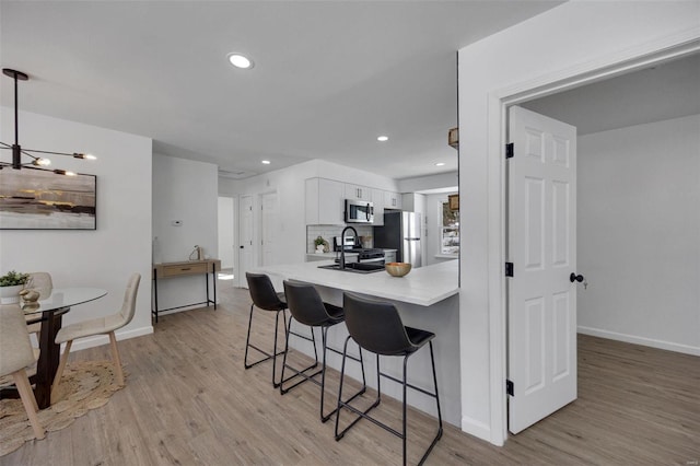 17 S Floridale Dr, Saint Louis, MO 63135 - kitchen with appliances with stainless steel finishes, a breakfast bar area, white cabinetry, light wood finished floors, and recessed lighting
