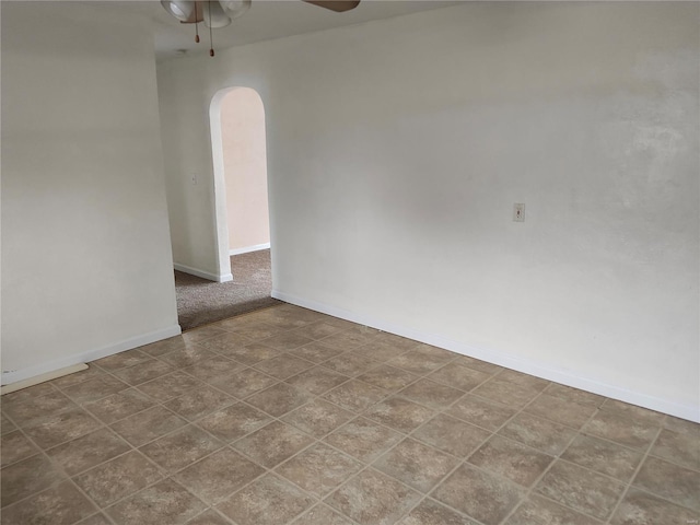 empty room featuring arched walkways, ceiling fan, and baseboards