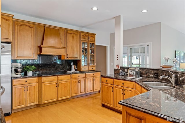 kitchen with premium range hood, a sink, freestanding refrigerator, light wood finished floors, and dark stone counters