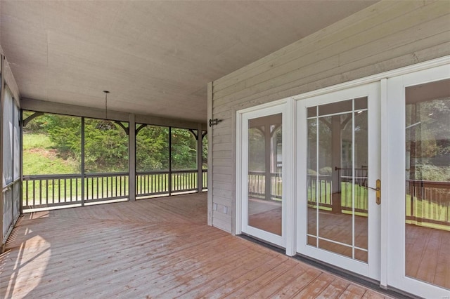 unfurnished sunroom with a deck, wood-type flooring, plenty of natural light, and wooden walls