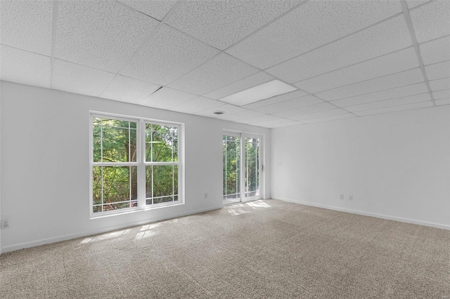 carpeted spare room with a drop ceiling and baseboards
