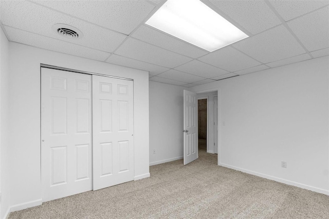 unfurnished bedroom with a paneled ceiling, carpet flooring, a closet, and baseboards