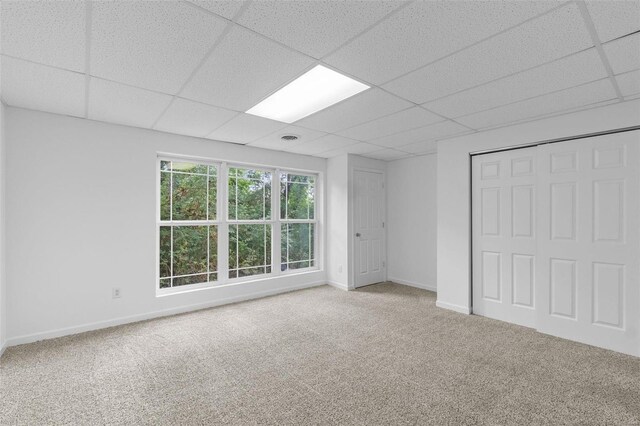 unfurnished bedroom with carpet floors, a drop ceiling, baseboards, and a closet