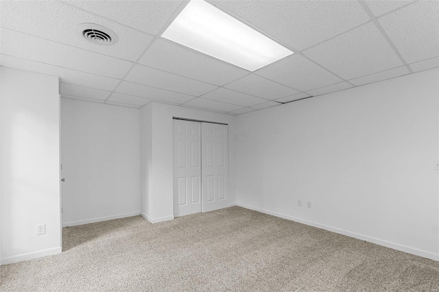 carpeted spare room featuring a drop ceiling and baseboards