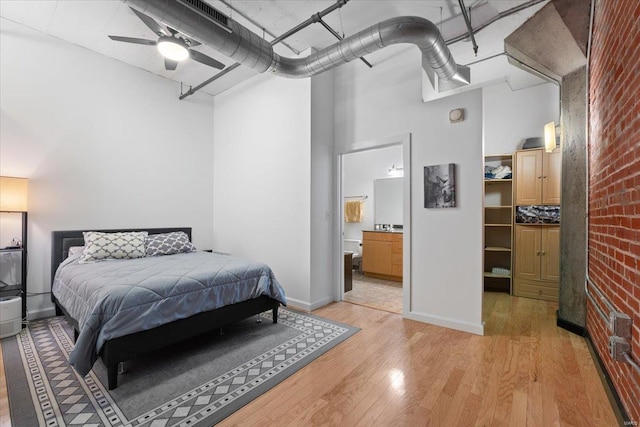 bedroom with a high ceiling, light wood-style floors, brick wall, ensuite bath, and baseboards
