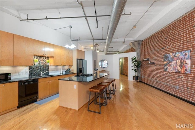 1619 Washington Ave Unit 805, Saint Louis, MO 63103 - kitchen featuring black appliances, brick wall, light wood finished floors, a kitchen island, and a kitchen bar