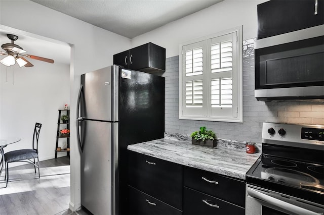 9154 Eager Rd, Saint Louis, MO 63144 - kitchen featuring stainless steel appliances, dark cabinets, a ceiling fan, tasteful backsplash, and light stone countertops