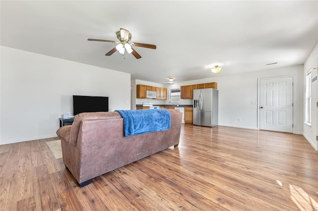 living room featuring a ceiling fan, light wood-style floors, and baseboards