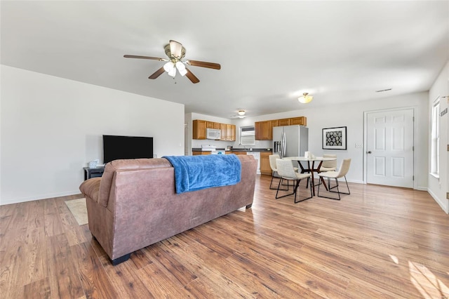 living area with ceiling fan, light wood-type flooring, and baseboards