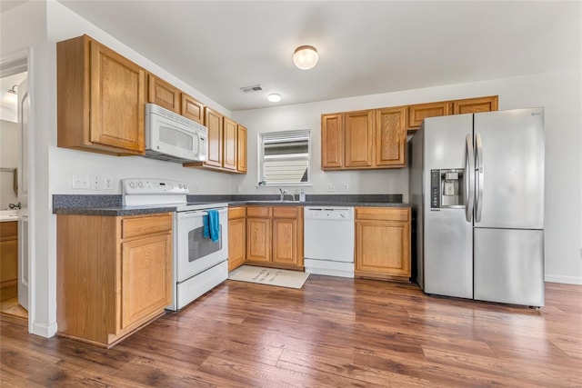 kitchen with white appliances, dark countertops, dark wood-style floors, and a sink