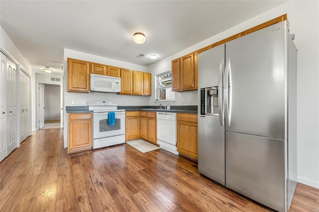 kitchen featuring white appliances, dark wood finished floors, dark countertops, baseboards, and a sink