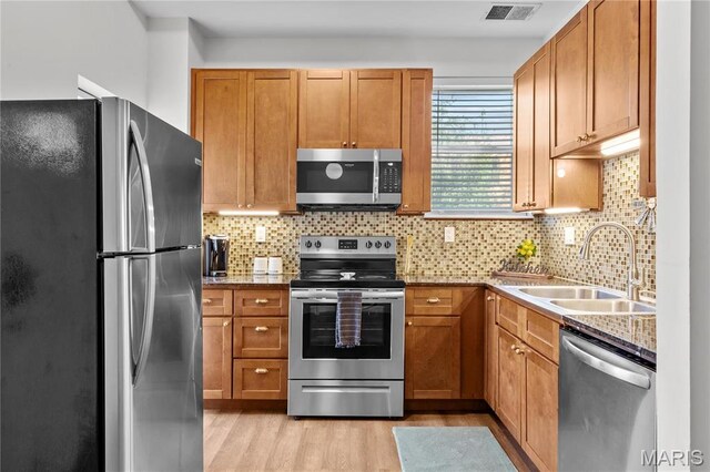 2005 Lynch St Unit C, Saint Louis, MO 63118 - kitchen featuring appliances with stainless steel finishes, a sink, light wood-style flooring, decorative backsplash, and brown cabinetry