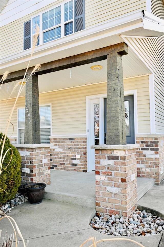 doorway to property with a porch and brick siding