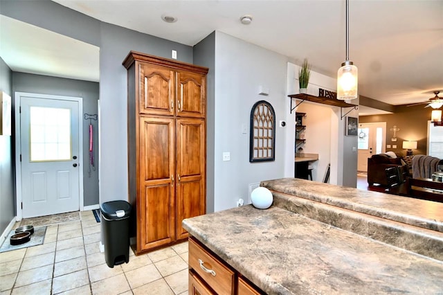 kitchen with brown cabinetry, light tile patterned floors, a ceiling fan, open floor plan, and pendant lighting