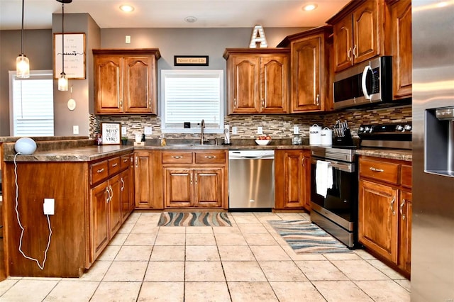kitchen with appliances with stainless steel finishes, a sink, dark countertops, a peninsula, and brown cabinets