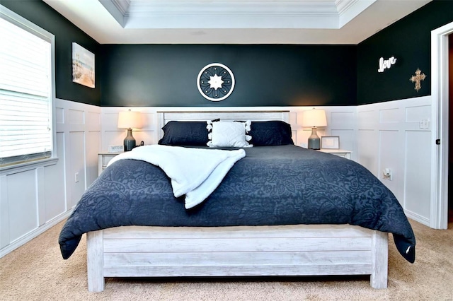 bedroom featuring ornamental molding, a decorative wall, a raised ceiling, carpet, and a wainscoted wall