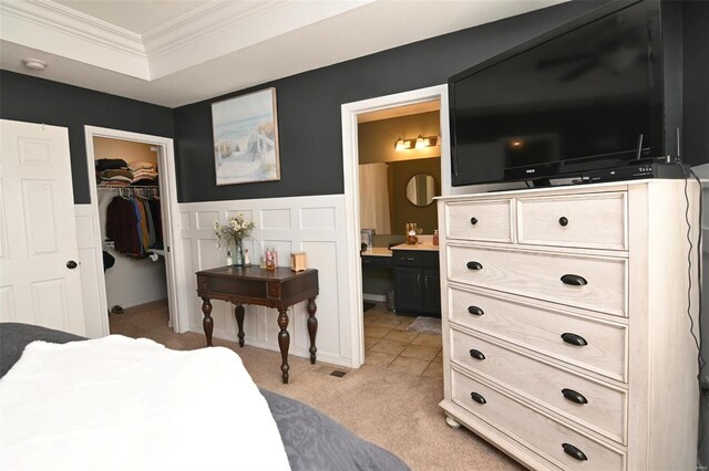 bedroom with crown molding, a walk in closet, light colored carpet, a closet, and wainscoting