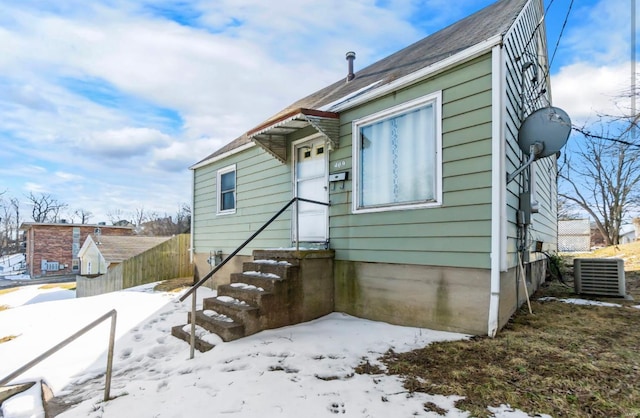 snow covered back of property featuring central AC, fence, and entry steps