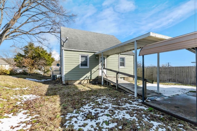 snow covered rear of property with fence, roof with shingles, and central AC unit