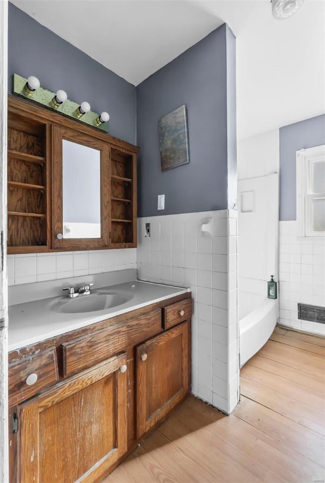 full bath with tile walls, wood finished floors, wainscoting, vanity, and a bath