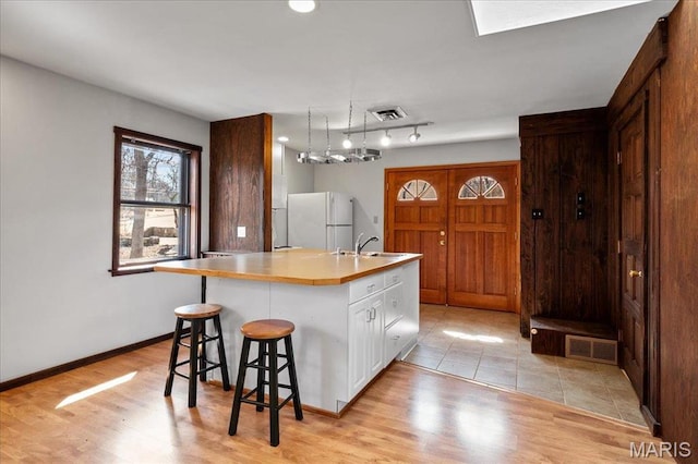 2013 Lily Ave, Saint Louis, MO 63122 - kitchen featuring freestanding refrigerator, white cabinets, an island with sink, a kitchen bar, and light wood-type flooring