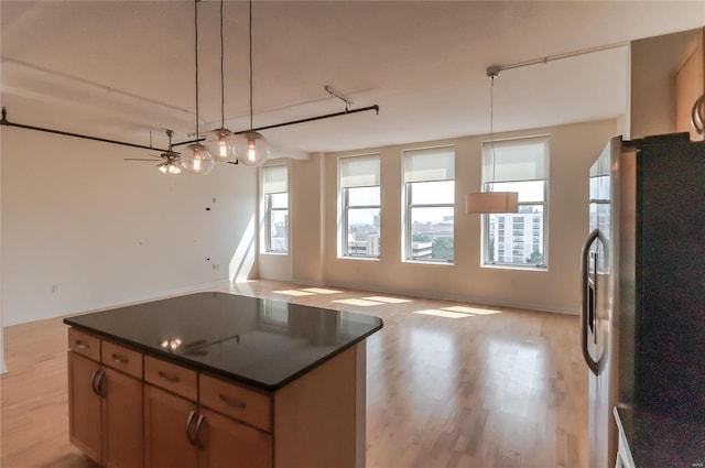 kitchen featuring stainless steel refrigerator with ice dispenser, dark countertops, open floor plan, hanging light fixtures, and a kitchen island