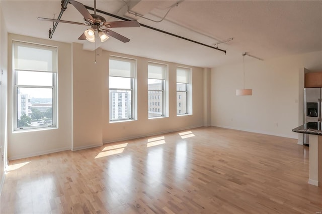 unfurnished living room featuring a ceiling fan, light wood-style floors, and baseboards