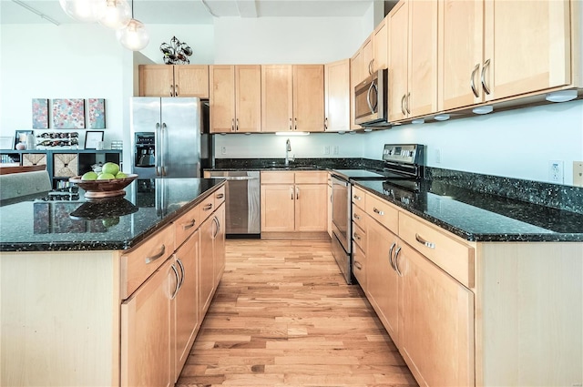 kitchen featuring appliances with stainless steel finishes, light wood-style flooring, light brown cabinetry, dark stone counters, and a center island