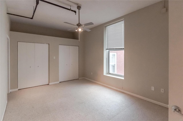 unfurnished bedroom featuring multiple closets, carpet flooring, baseboards, and ceiling fan
